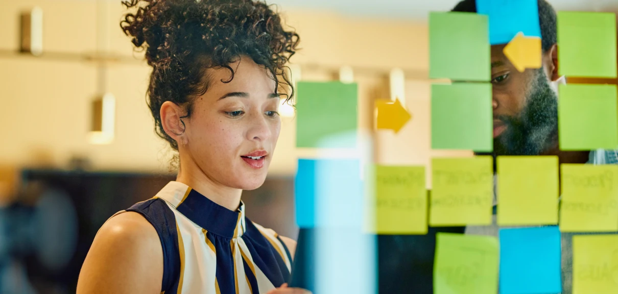 Woman standing in front of a wall covered in post-it notes, looking intently at one of the notes